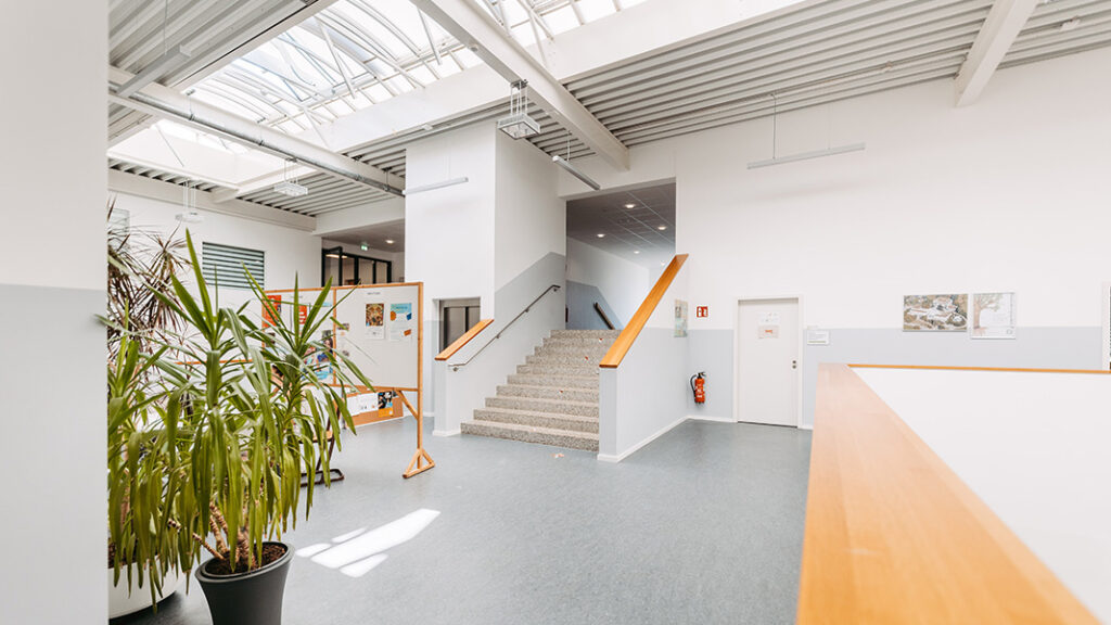 Heller Eingangsbereich mit Treppe, großen Pflanzen in Töpfen und einer Pinnwand.