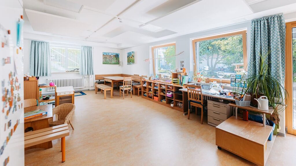 Ein leerer Aufenthaltsraum der mit zwei Sitzecken, einem Schreibtisch und mehreren Regalen voller Spiele ausgestattet ist.