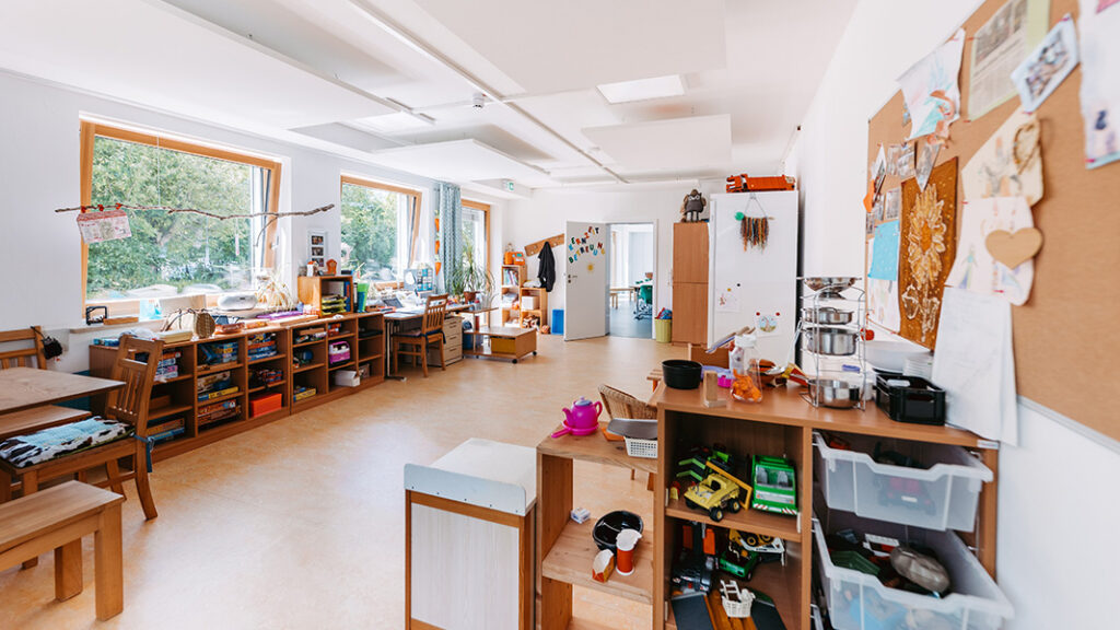 Ein leerer Aufenthaltsraum der mehrere Regale voller Spielzeuge enthält und bunt dekoriert ist.