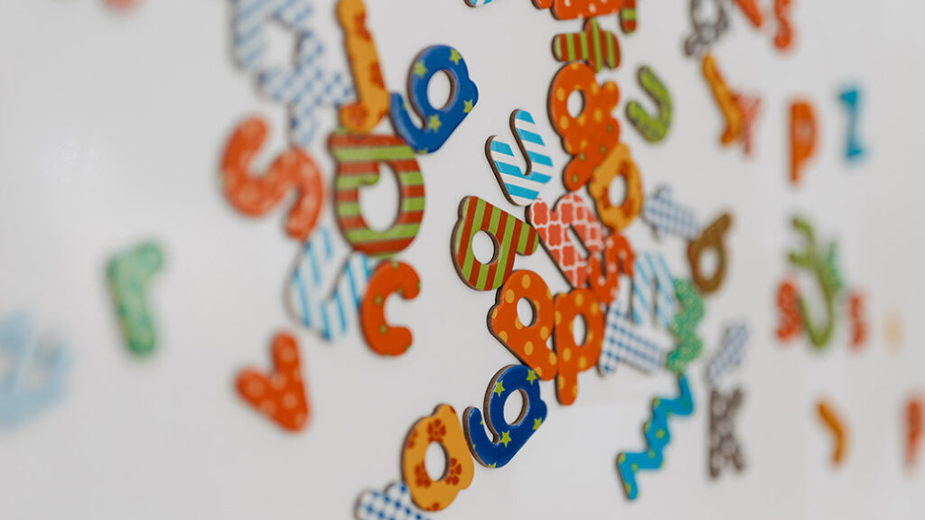 Bunte, gemusterte Buchstaben aus Holz oder Kunststoff, lose auf hellem Untergrund verteilt.