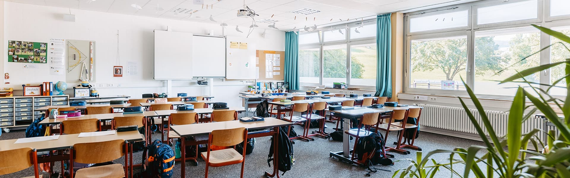 Leeres Klassenzimmer mit mehreren Tischreihen mit den Schulranzen der Schüler an den Tischen und mit Blick auf die Tafel