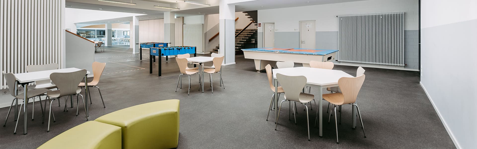 Leerer Aufenthaltsbereich mit einer grünen Sitzecke, Tischen und einem Tischkicker sowie einer Tischtennisplatte