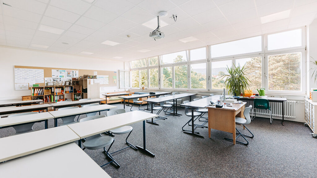 Modernes, helles leeres Klassenzimmer mit mehreren Tischreihen und Blick auf eine Pinnwand