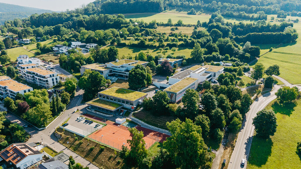 Luftaufnahme auf das moderne Gebäudekomplex der Messelbergschule, drum herum sind grüne Felder und Bäume zu sehen