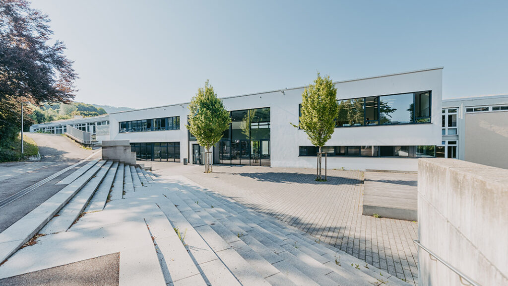 Leerer Schulhof aus Blick von einer Treppe mit zwei grünen Bäumen im Schulhof