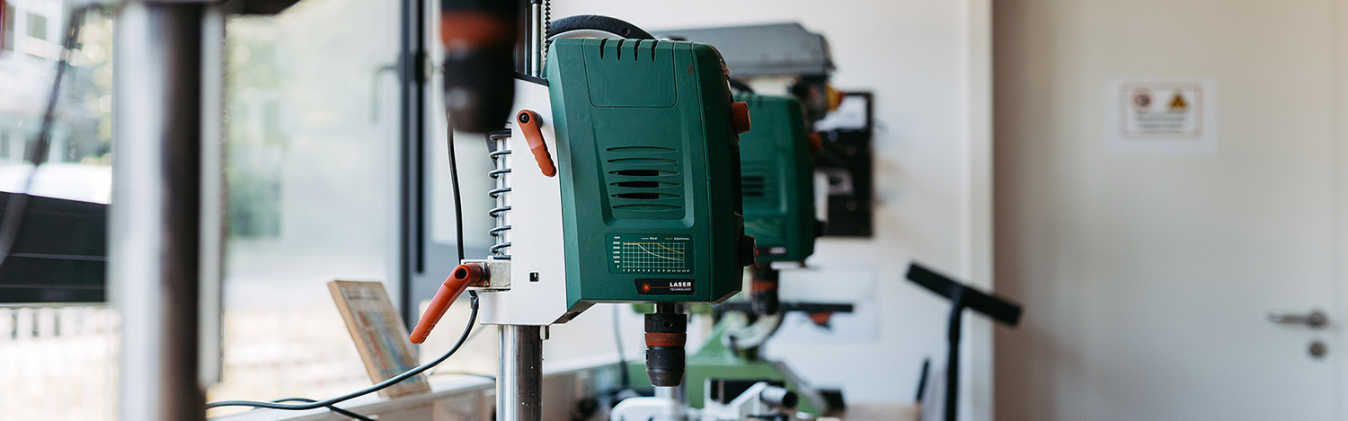 Bohrmaschine mit grünem Gehäuse und orangefarbenem Kabel an einer Werkbank in Werkstatt