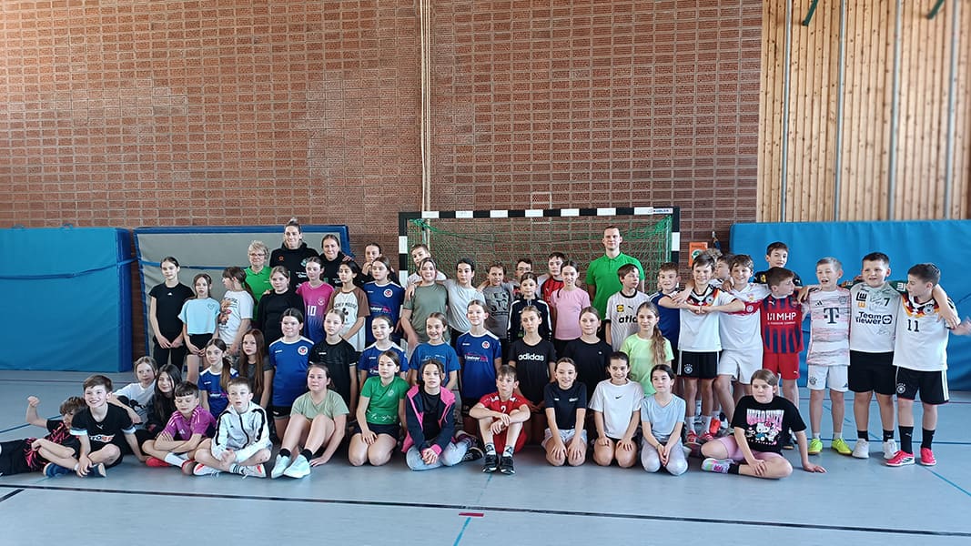Große Gruppe von Kindern und Jugendlichen in Sportkleidung vor einem Handballtor in einer Sporthalle